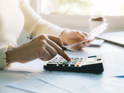 Hands using a calculator and writing on papers beside a laptop at a desk
