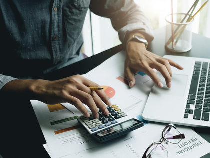 Hands using calculator and laptop on desk with charts and glasses