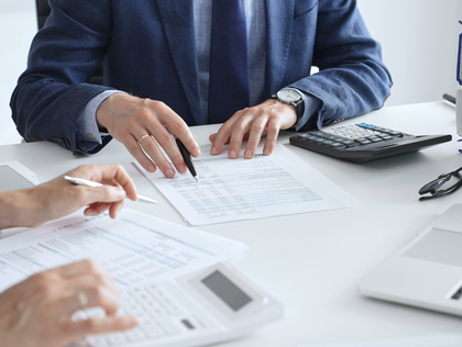 People reviewing printed documents at a white office table with a calculator and laptop