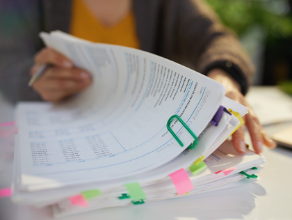 Hands flipping through a thick stack of clipped printed documents with colorful sticky tabs