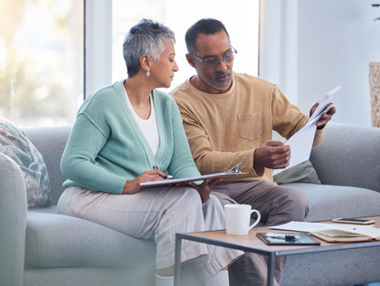 Two people reviewing papers on a couch in a bright living room with a coffee mug and notebook on a table