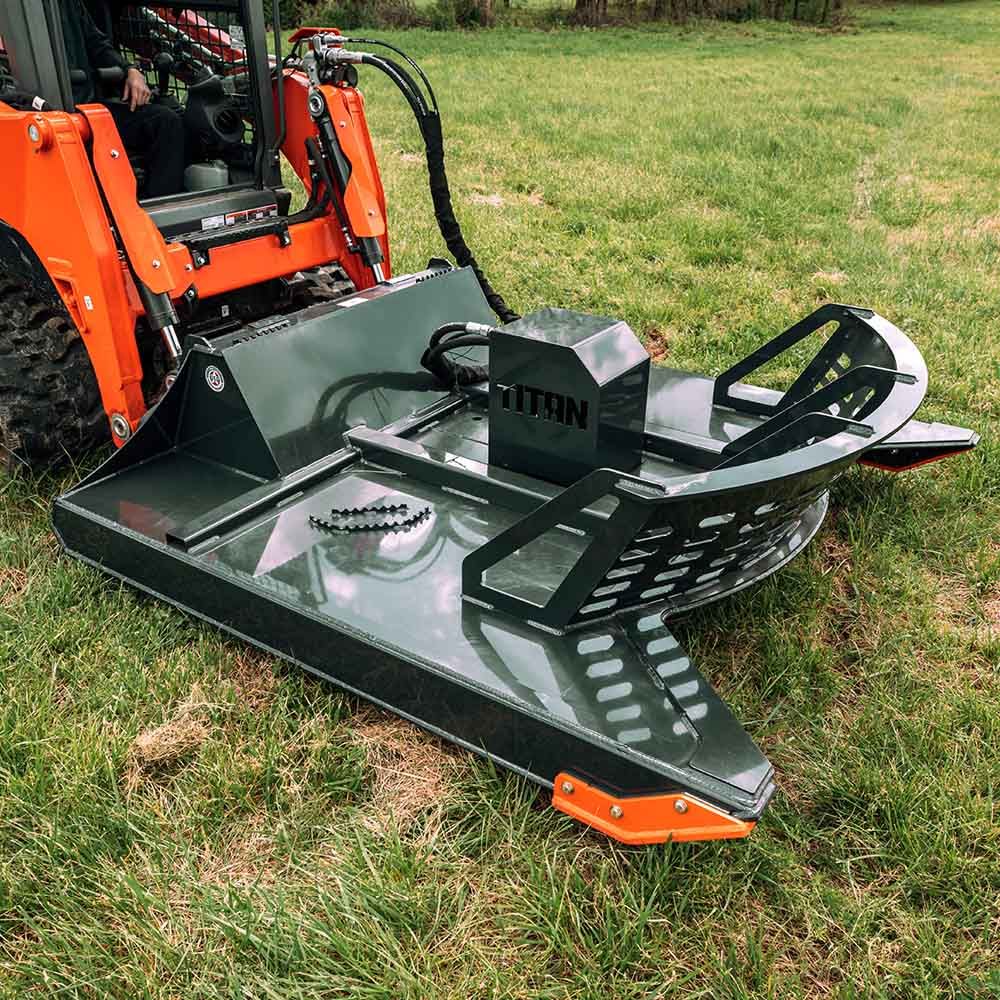 A heavy-duty, dark grey skid steer brush cutter attachment by Titan, mounted on an orange machine in a grassy field.