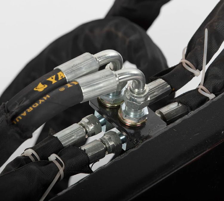A close-up of industrial hydraulic hoses and metal fittings connected to a black mounting plate on equipment.