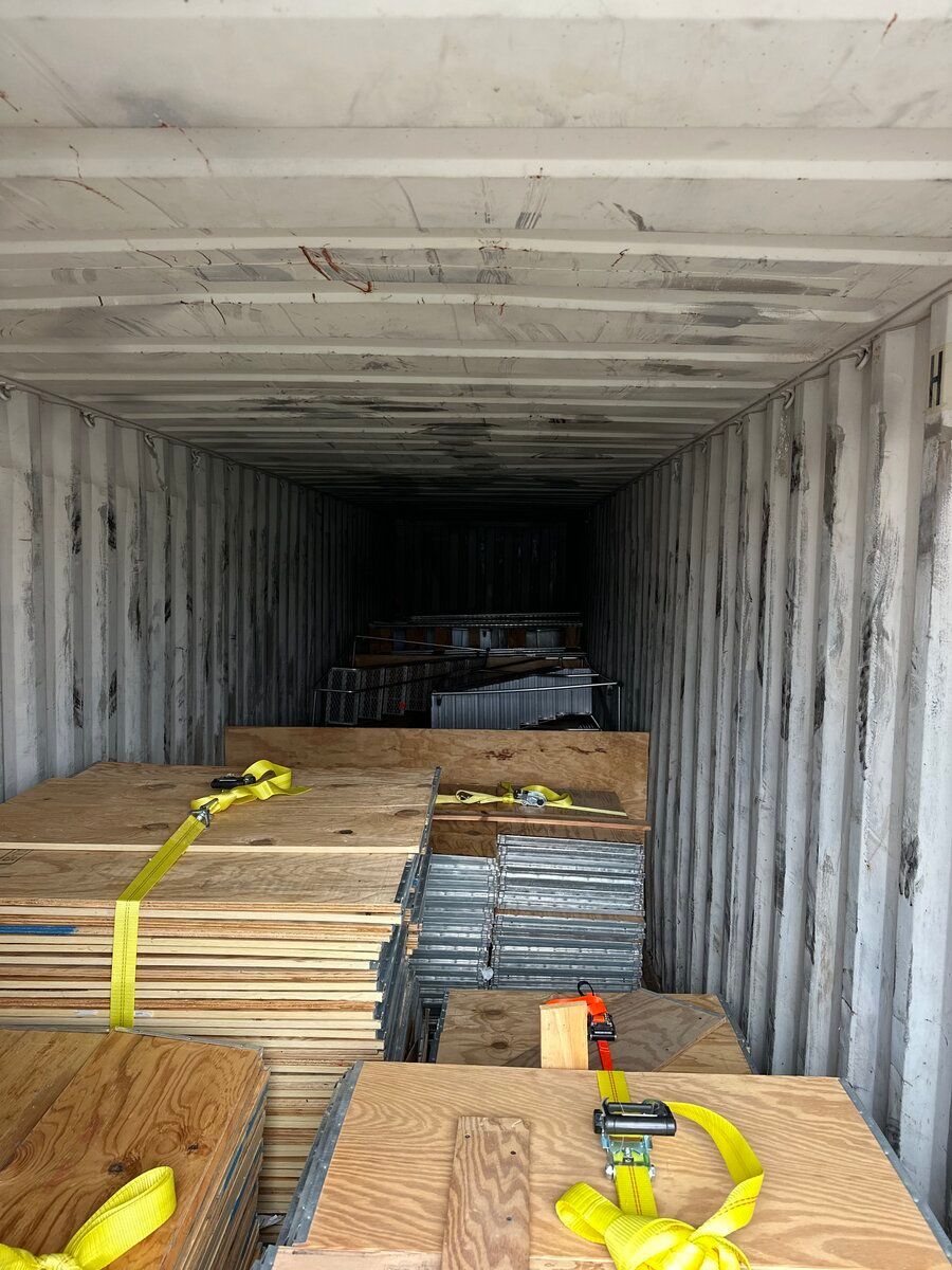Inside of a cargo shipping container featuring stacked wooden panels and metallic materials secured with yellow straps.