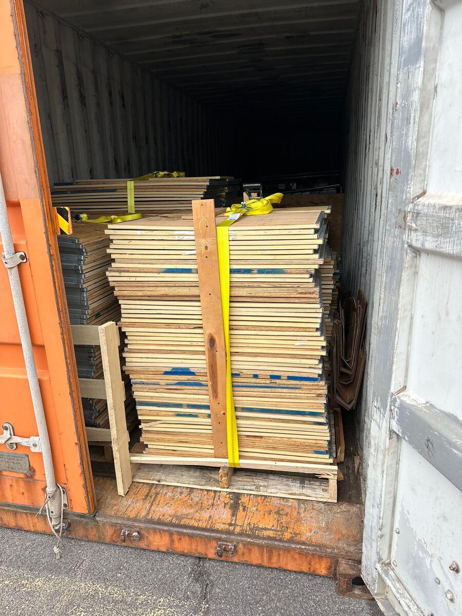 A stack of wooden boards secured with a yellow strap on a pallet inside an orange shipping container.