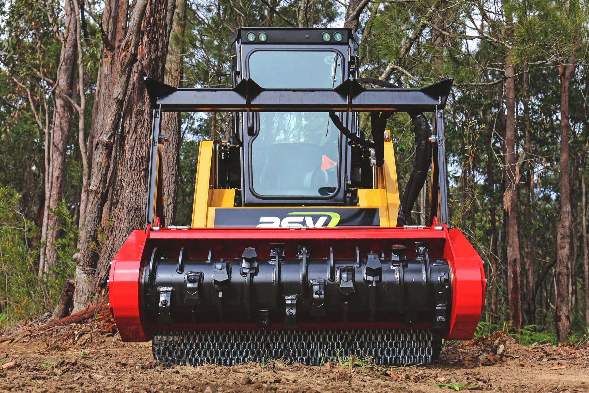 A yellow ASV skid steer loader with a large red industrial forestry mulcher attachment, positioned in a wooded area.
