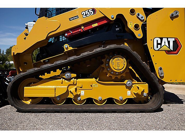 Side view of the yellow tracks and undercarriage of a CAT 255 compact track loader on a gravel surface.