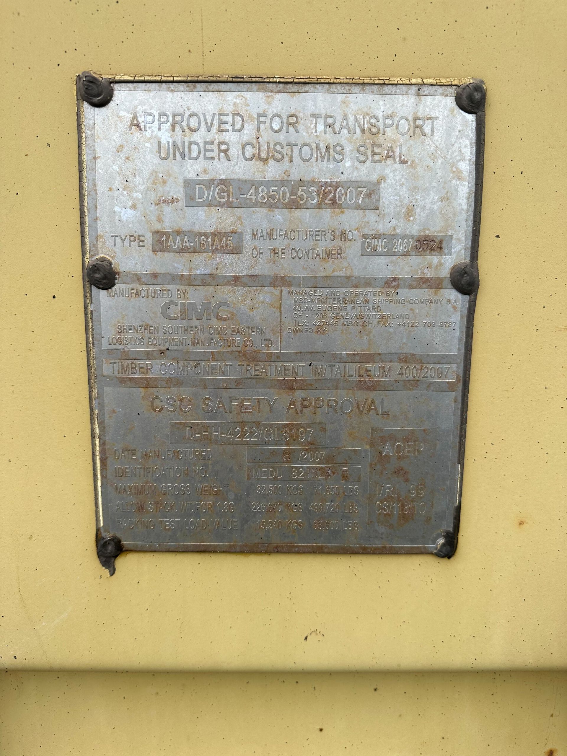 A weathered metal certification plate for international transport under customs seal attached to a yellow container.
