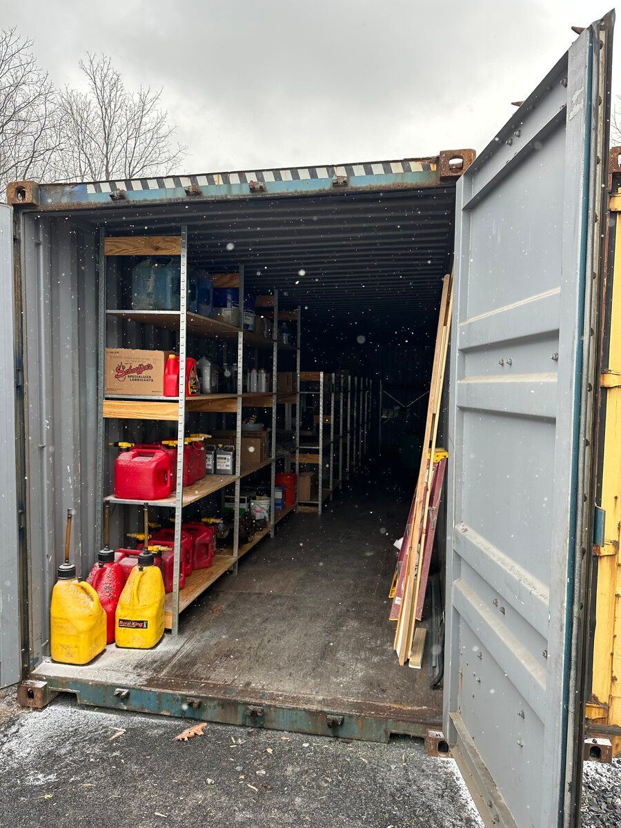 An open storage shipping container featuring tall metal shelving units filled with various containers and red gas cans.