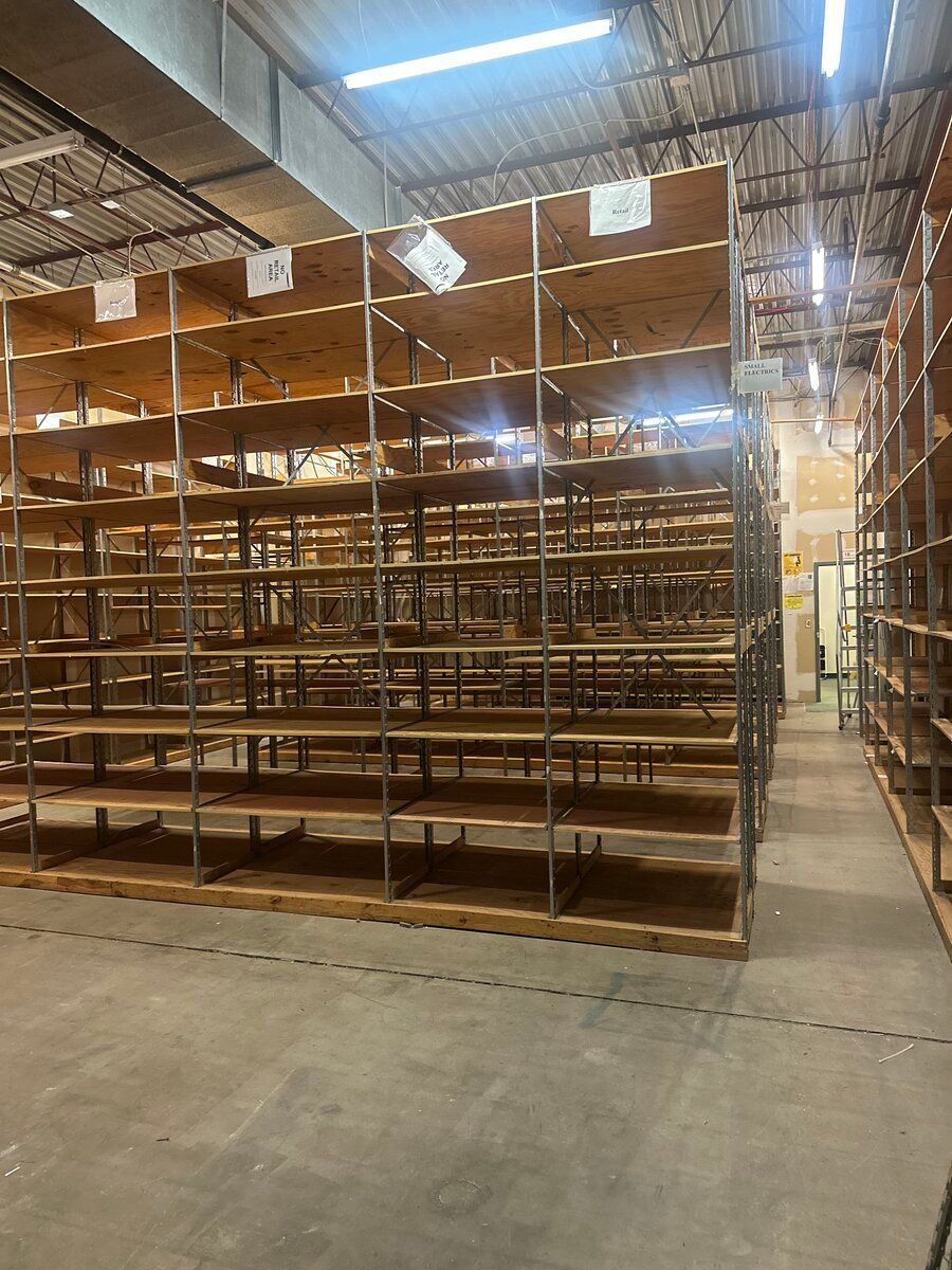 Rows of empty industrial wooden shelving units in a warehouse with high ceilings and overhead lighting.