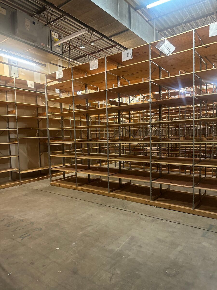 Empty industrial metal shelving units span a warehouse wall under bright overhead lighting.
