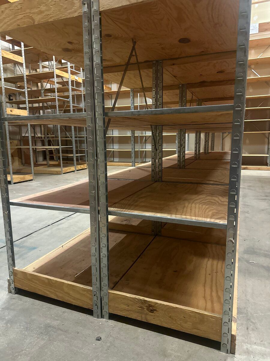 Empty, multi-level industrial shelving units constructed from metal frames and plywood shelves in a warehouse.