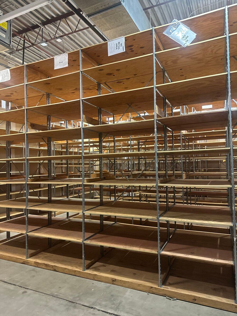 Empty, tall wooden shelves with metal supports stand in a warehouse with an exposed ceiling.