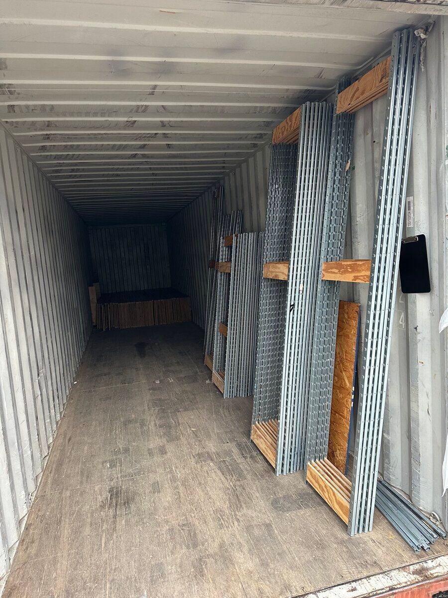 Inside a shipping container, metal construction studs are braced against the side wall using wooden framing.