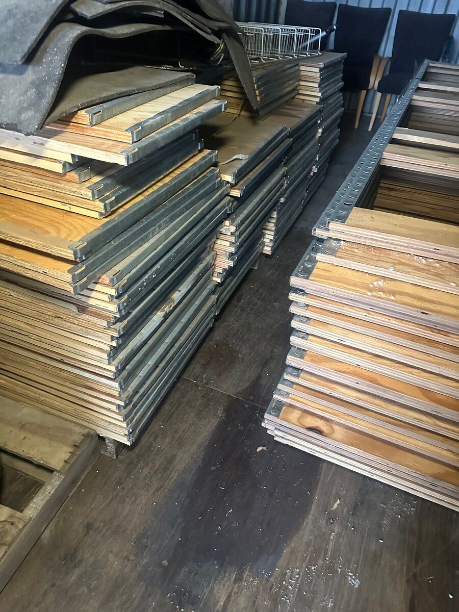 Stacks of wooden scaffolding planks with metal edges are arranged in rows on a floor.