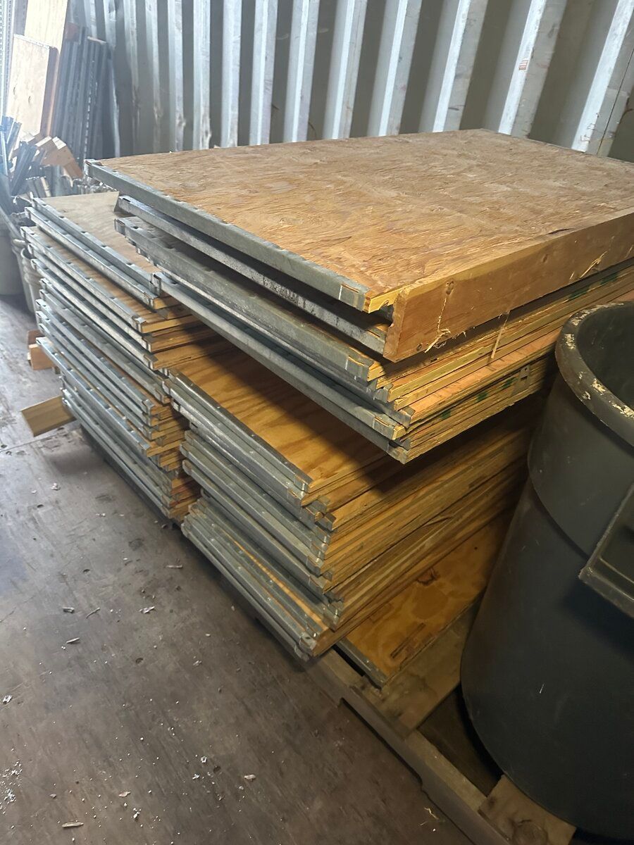 A stack of wood-paneled floor segments with metal edging rests on a pallet inside a warehouse.