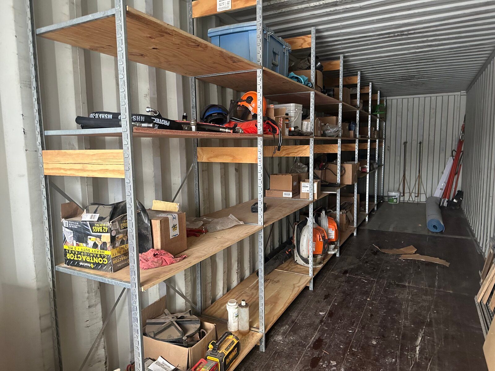 A long metal shelving unit filled with various tools and boxes inside a large, corrugated metal storage container.