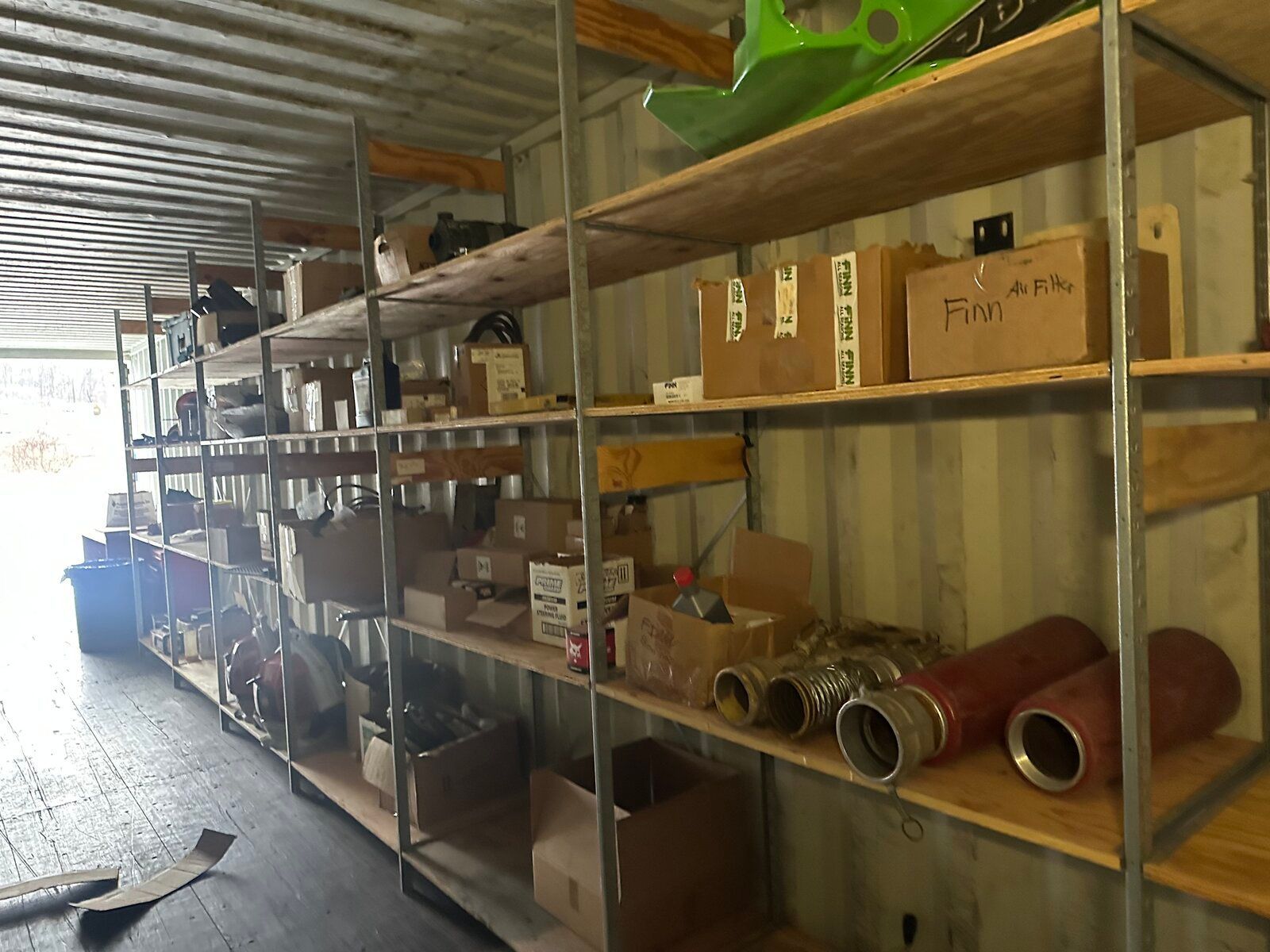 Storage shelves inside a corrugated metal shipping container filled with assorted boxes, pipes, and equipment.