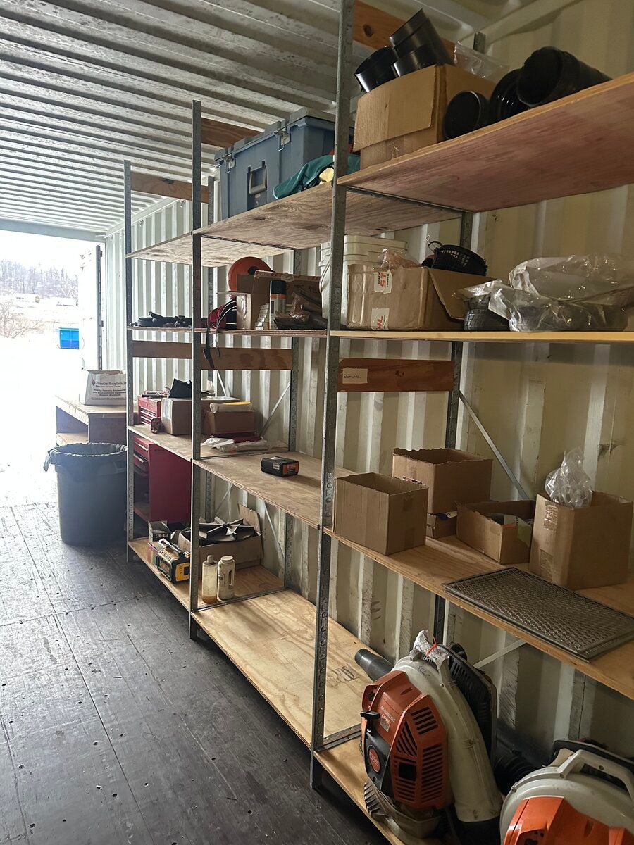 Metal shelving units filled with various tools, boxes, and equipment inside a storage container.