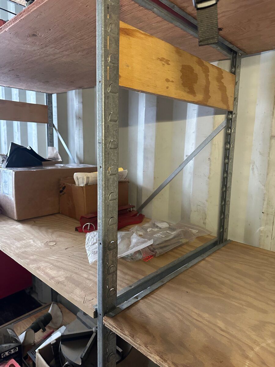 Metal shelving unit with plywood shelves inside a corrugated container, with a cardboard box and stored items on display.