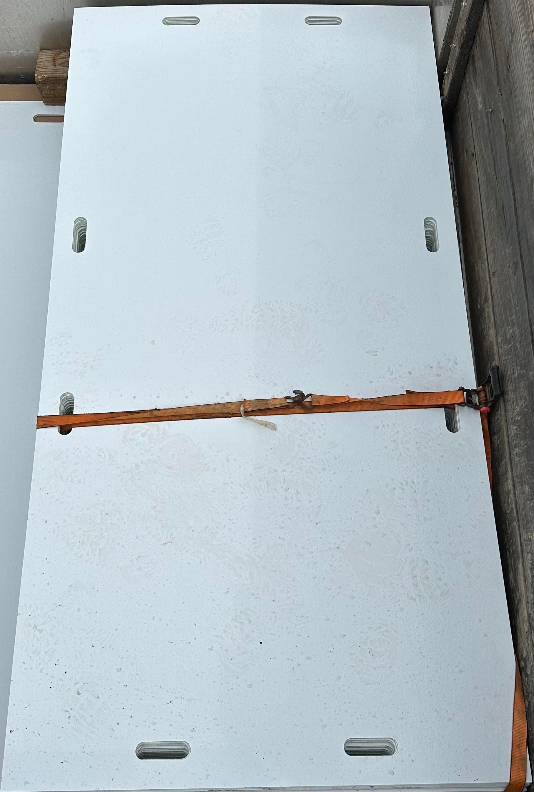 A stack of rectangular, light gray concrete panels with embedded metal loops, secured together by an orange strap.