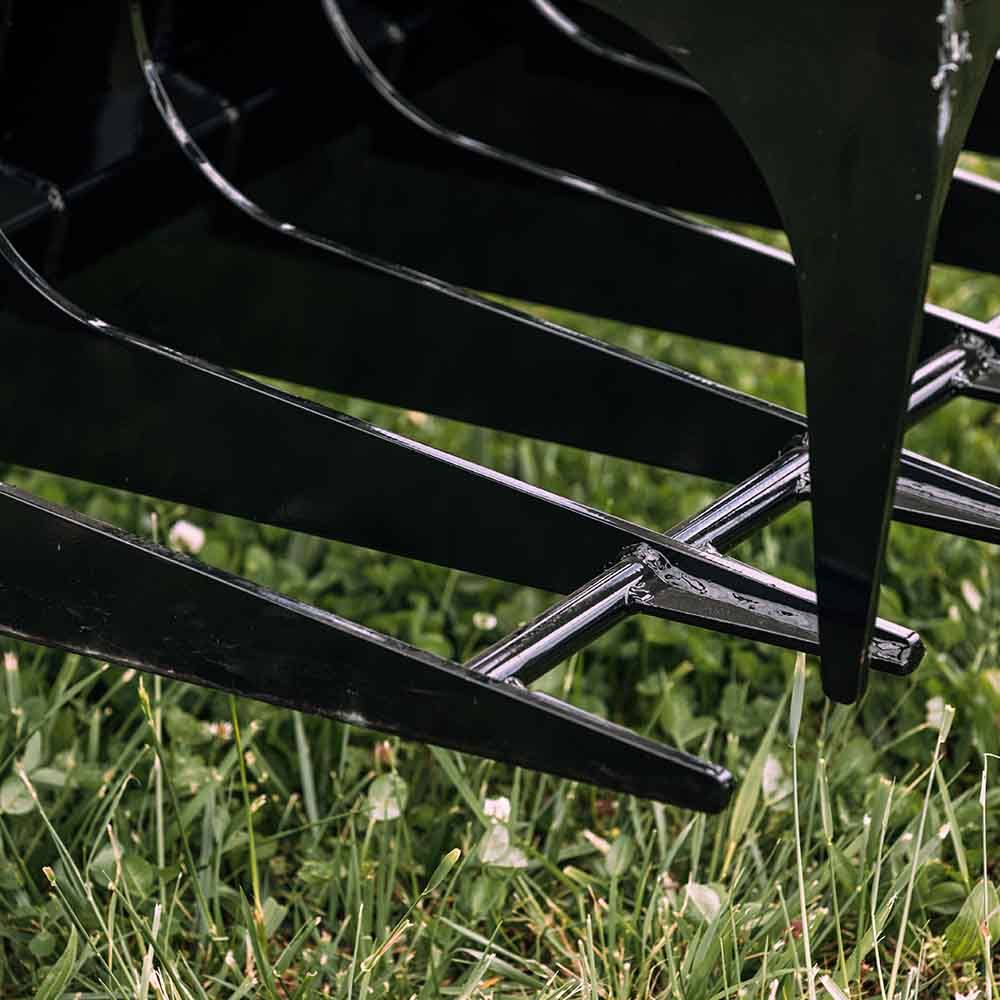Black metal rake tines of a tractor implement resting in a green grass field.