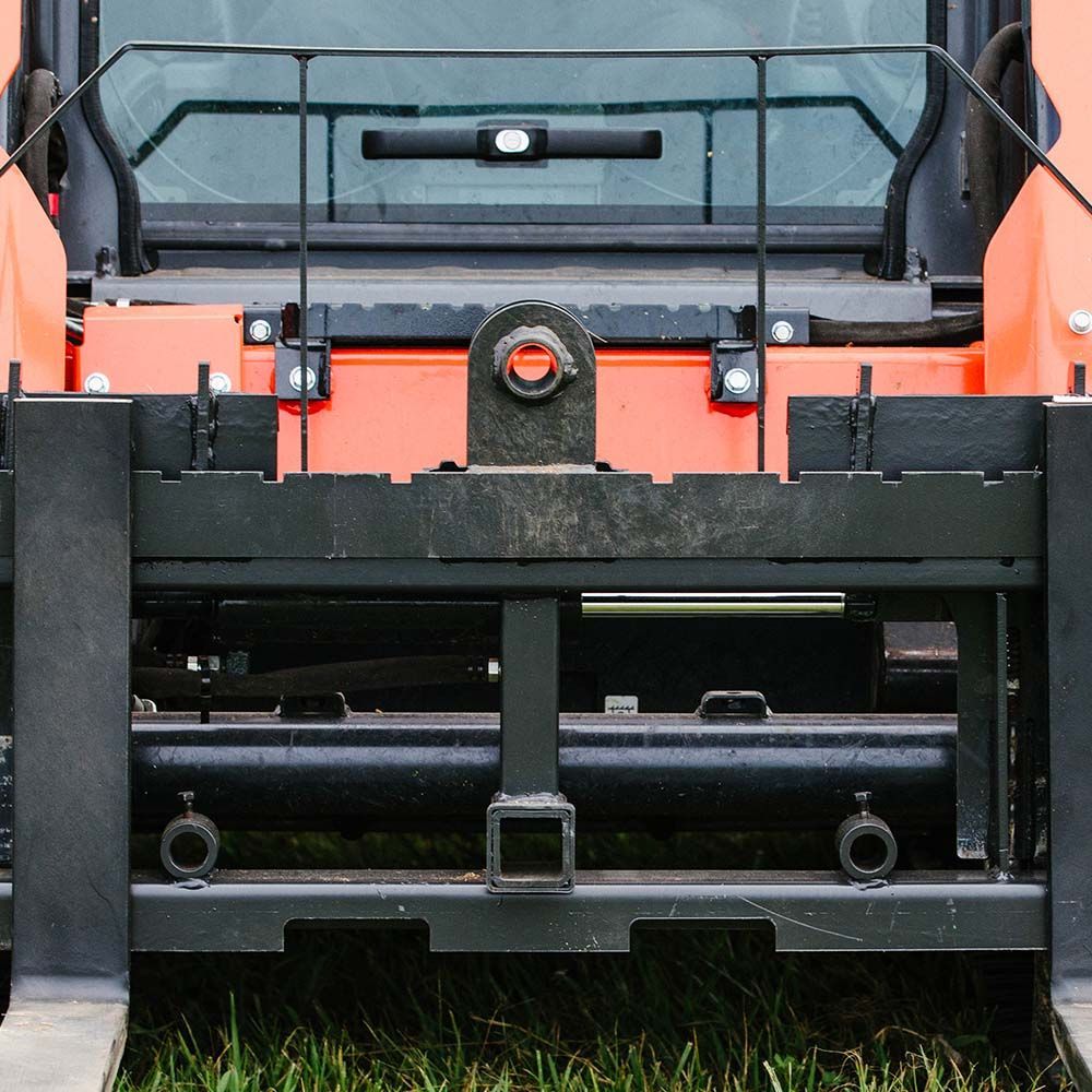 Close-up of a black metal forklift attachment mounted on the front of an orange construction vehicle.