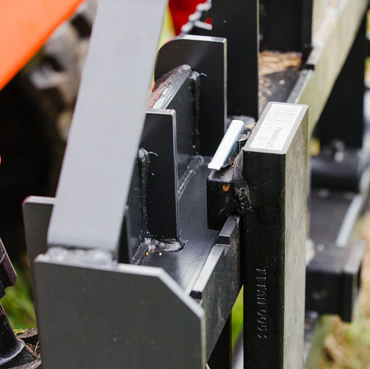Close-up of a black metal tractor attachment component with visible welds and a stamped brand logo, outdoors.