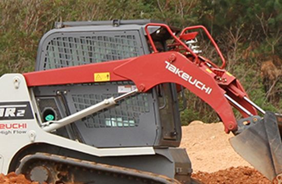 A red and white Takeuchi skid steer loader moves dirt on a construction site.