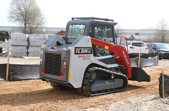 A white and red Takeushi TL8R2 compact track loader parked on a dirt construction site.
