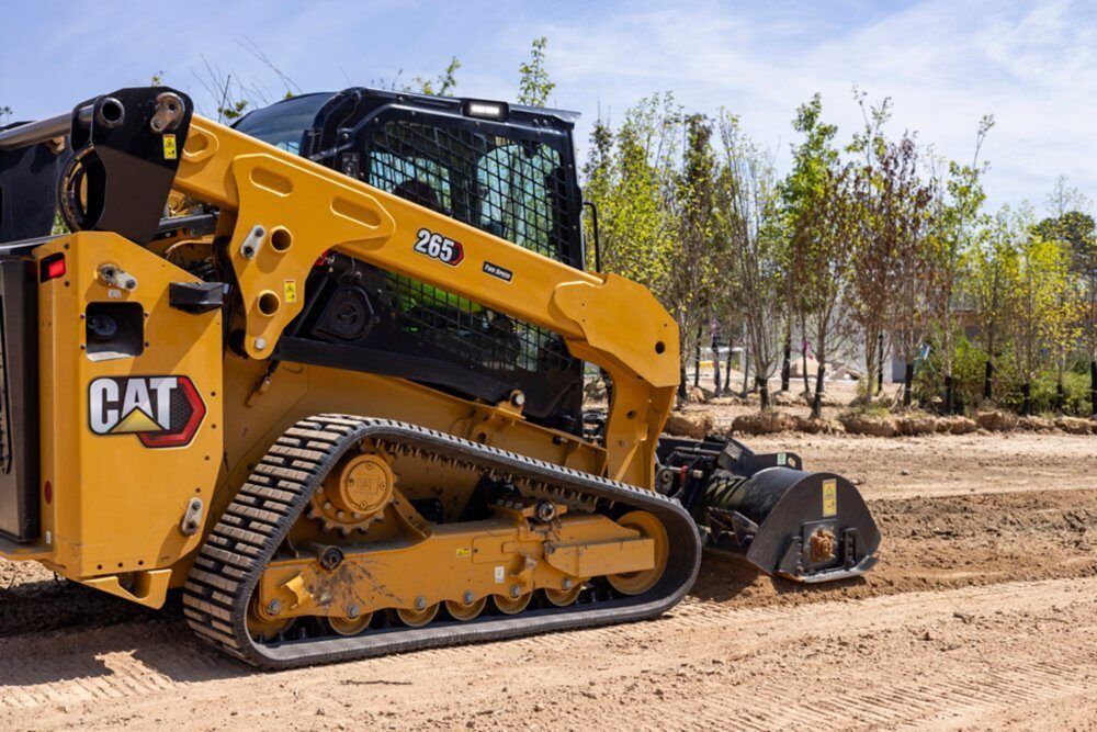 A yellow and black ASV compact track loader sits on a flatbed trailer in front of industrial buildings under a cloudy sky.