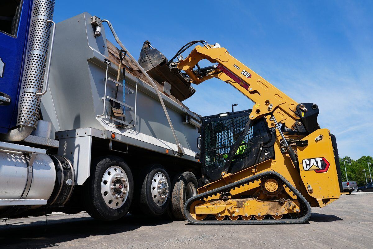 A yellow and black ASV compact track loader with a bucket attachment parked on dirt outside an industrial building.