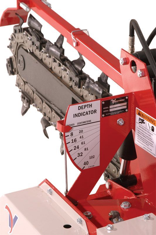 A close-up of a red trencher machine featuring a depth indicator gauge labeled with measurements in inches.