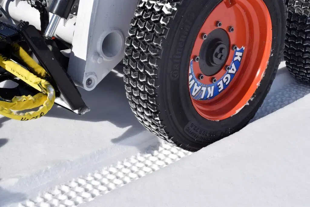 A close-up of a heavy-duty tire with aggressive tread marks traveling through fresh snow, leaving a patterned track behind.