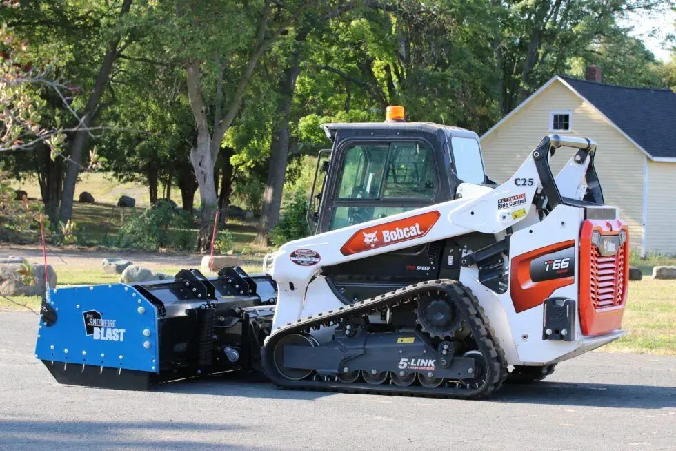A white and orange Bobcat compact track loader with a blue Kage Snowfire Blast attachment outdoors.