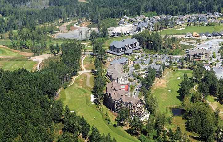 Aerial view of a mountain resort with buildings, parking lots, green slopes, and forested surroundings