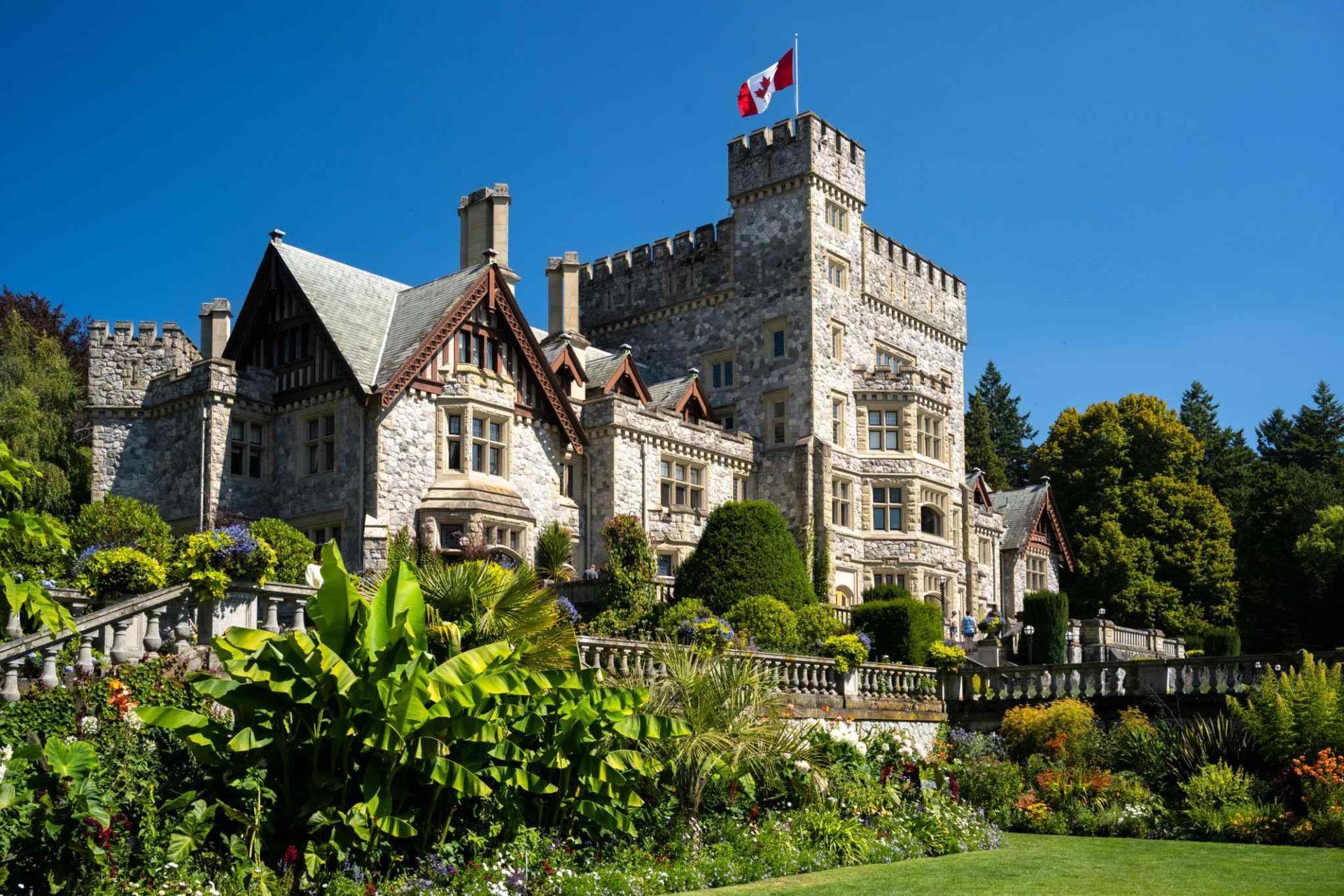 Stone castle with a Canadian flag, surrounded by lush green gardens under a bright blue sky