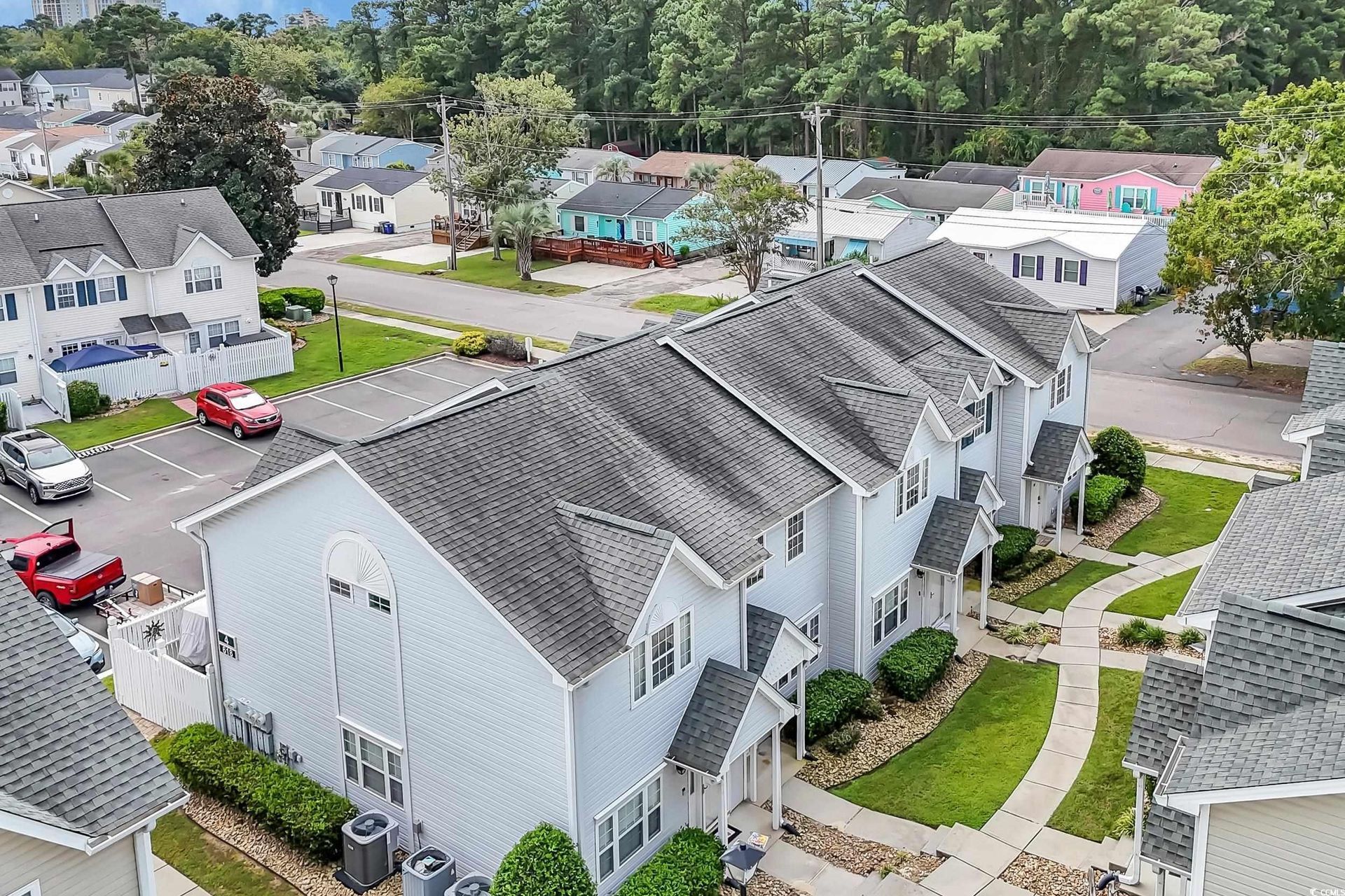 Aerial view of townhouses with dark gray roofs, green lawns, and colorful houses in the background.