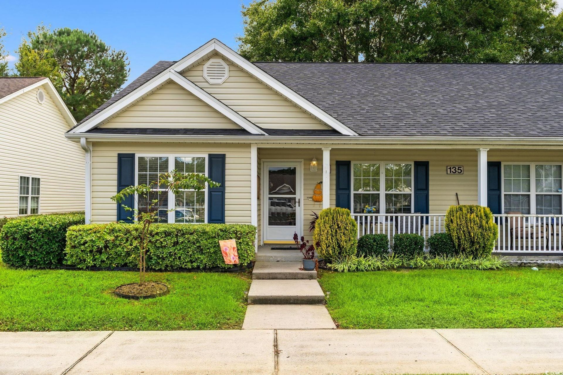 Beige house with blue shutters, a porch, and green lawn.