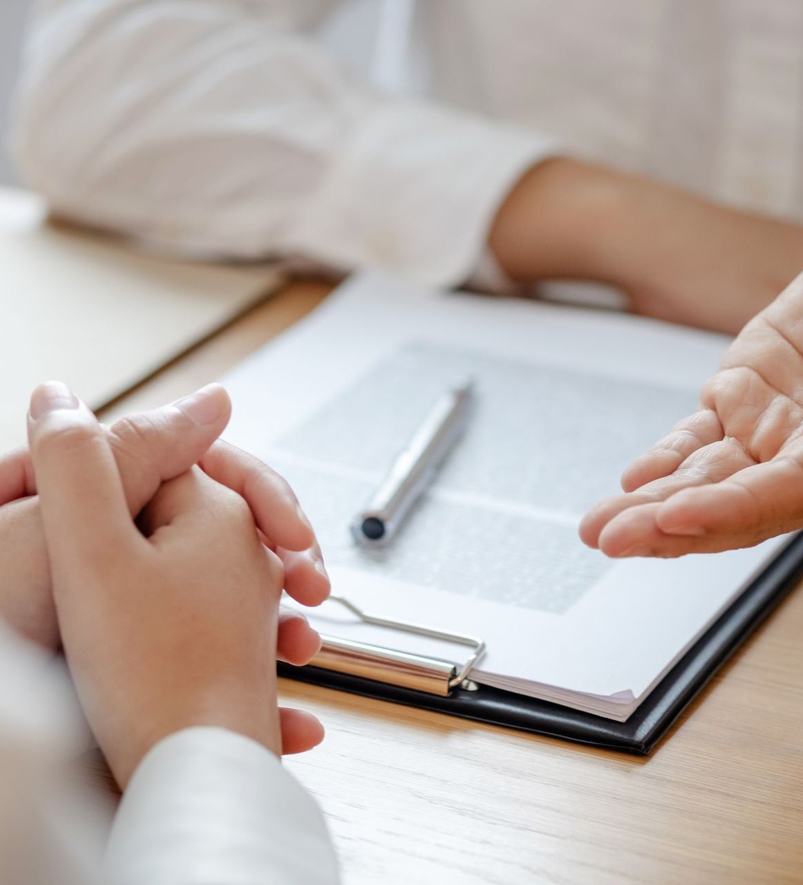 A person is sitting at a table with a clipboard and a pen.