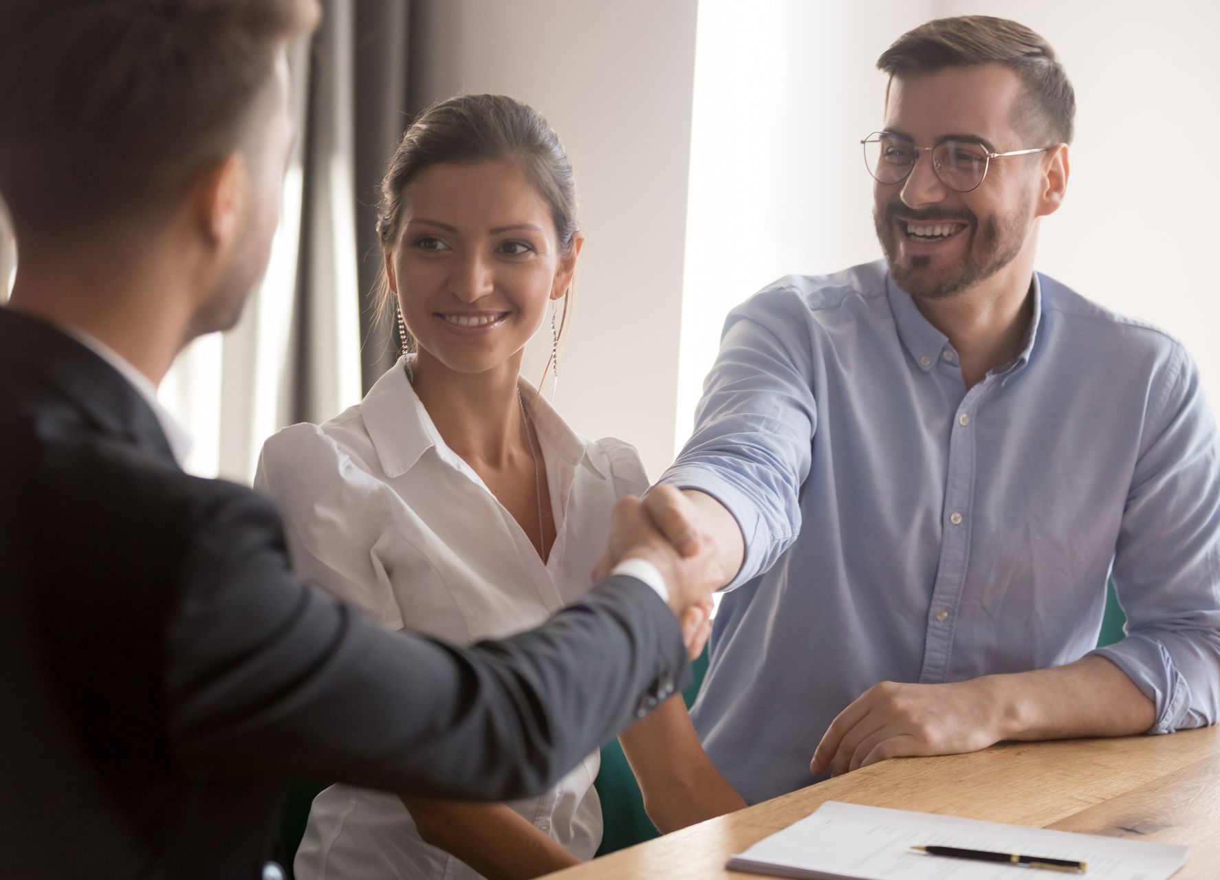 A man and a woman are shaking hands while sitting at a table.