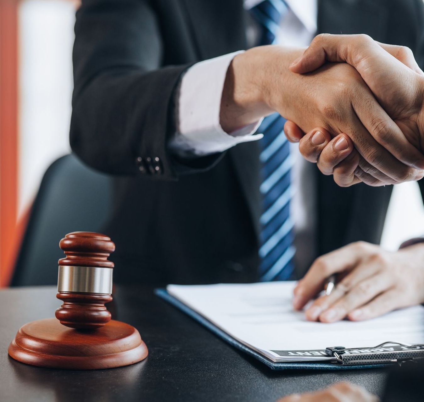 Two men shaking hands in front of a judge's gavel.