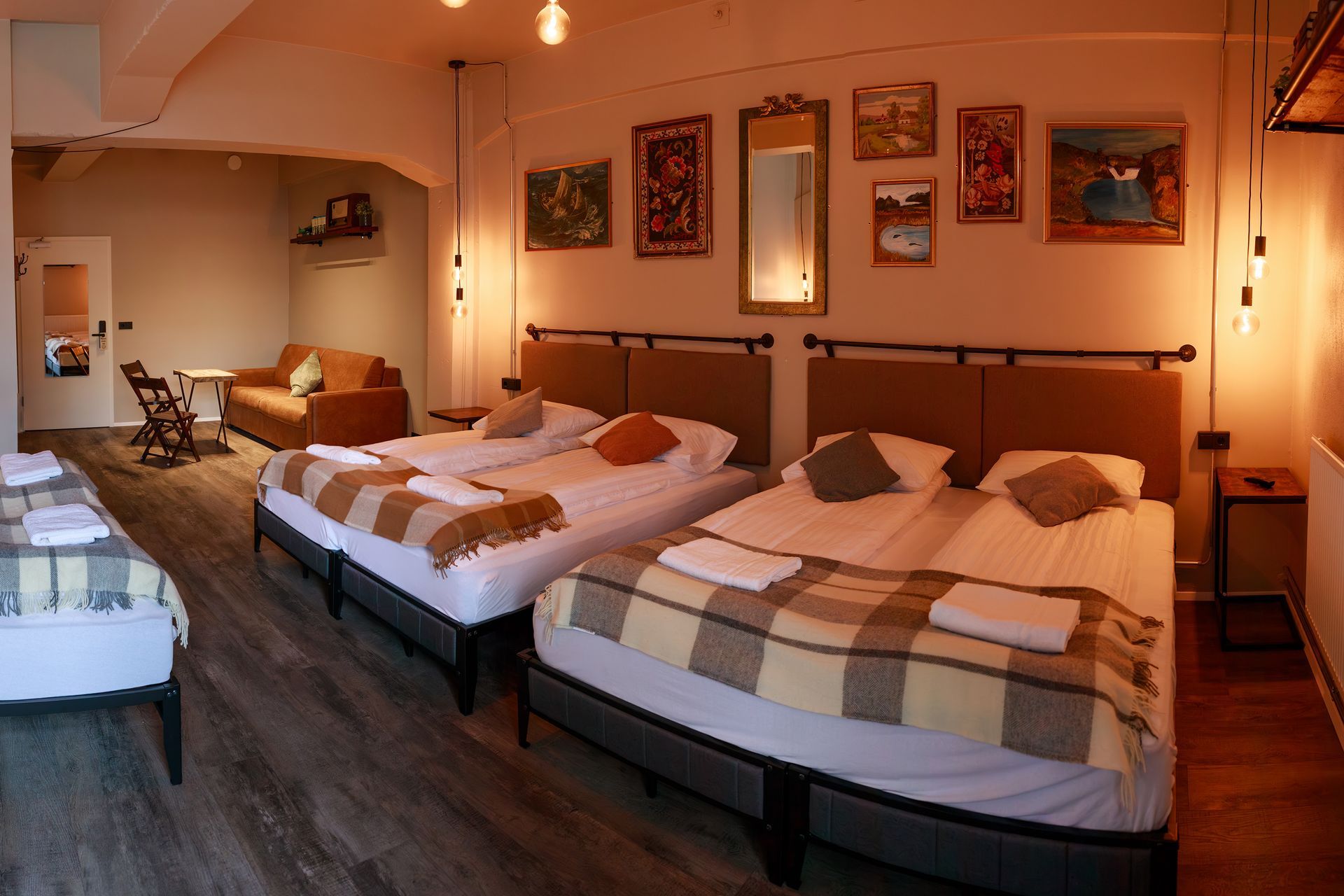 Spacious hotel room with three beds, a couch, artwork, and warm lighting.
