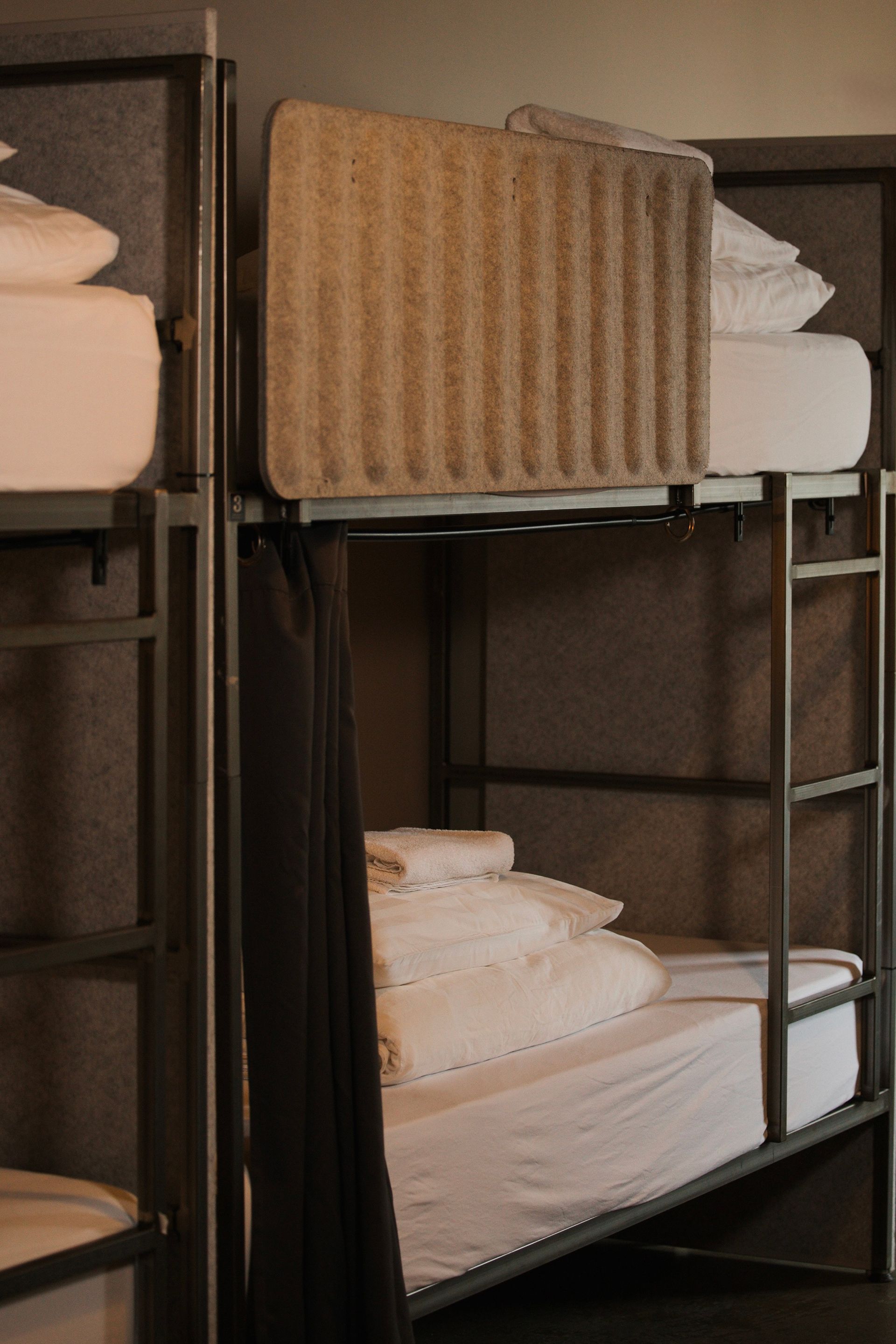 Bunk beds in a room with white bedding and gray metal frames. A curtain hangs on one bunk.