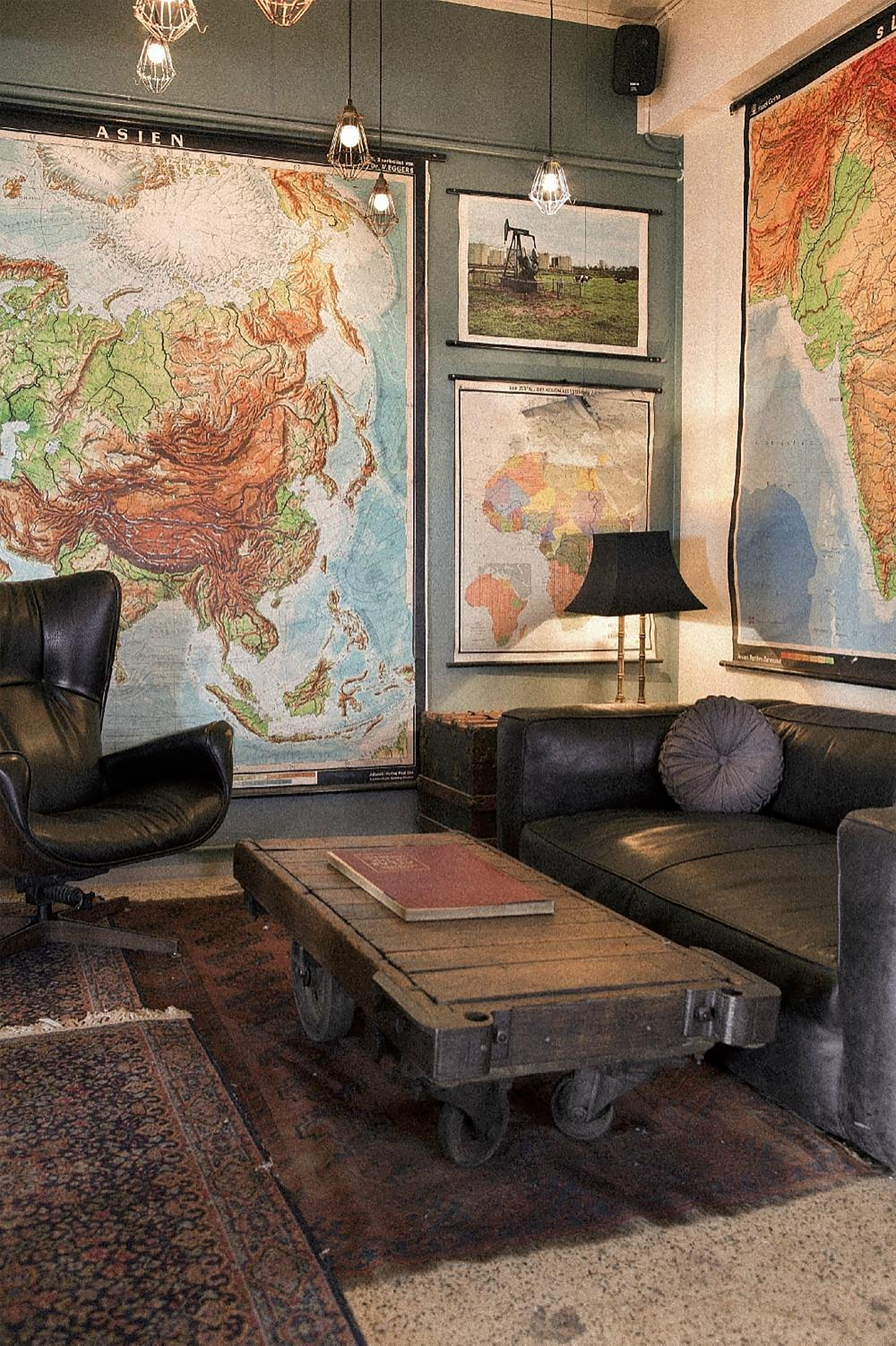 Living room with maps on the wall, dark leather furniture, and a wooden coffee table.