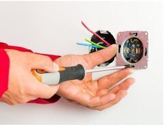 Electrician installing a electrical outlet using a screwdriver.