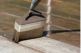 Picture of a handyman Richmond worker conducting deck and patio maintenance by sanding off the old finish. The worker is using a yellow palm sander and is wearing shorts.