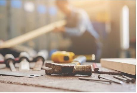 Handy worker repairing structural walls. The worker is wearing blue overalls and is sanding a wood beam.