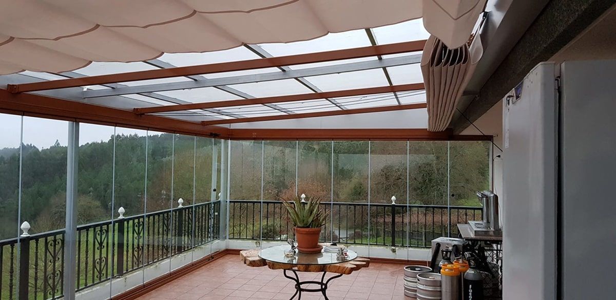 Terraza acristalada con paredes de cristal, estructura de madera y vistas a los árboles.