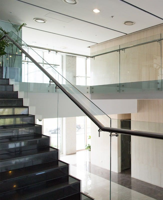 Escalera con escalones de mármol negro, barandillas de cristal e interior de oficina moderno.